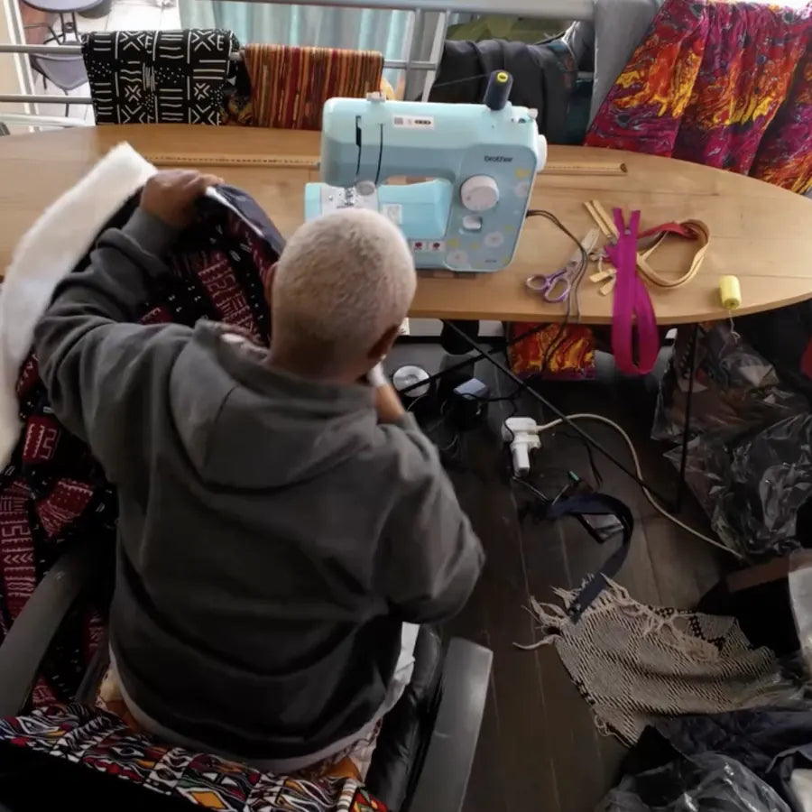 Cecilia at her sewing table, working on a piece surrounded by African print fabrics.